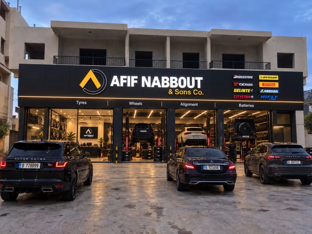 Afif Nabbout & Sons Co. branch in Batroun, with its sign lit above the open service bays and three cars parked in front